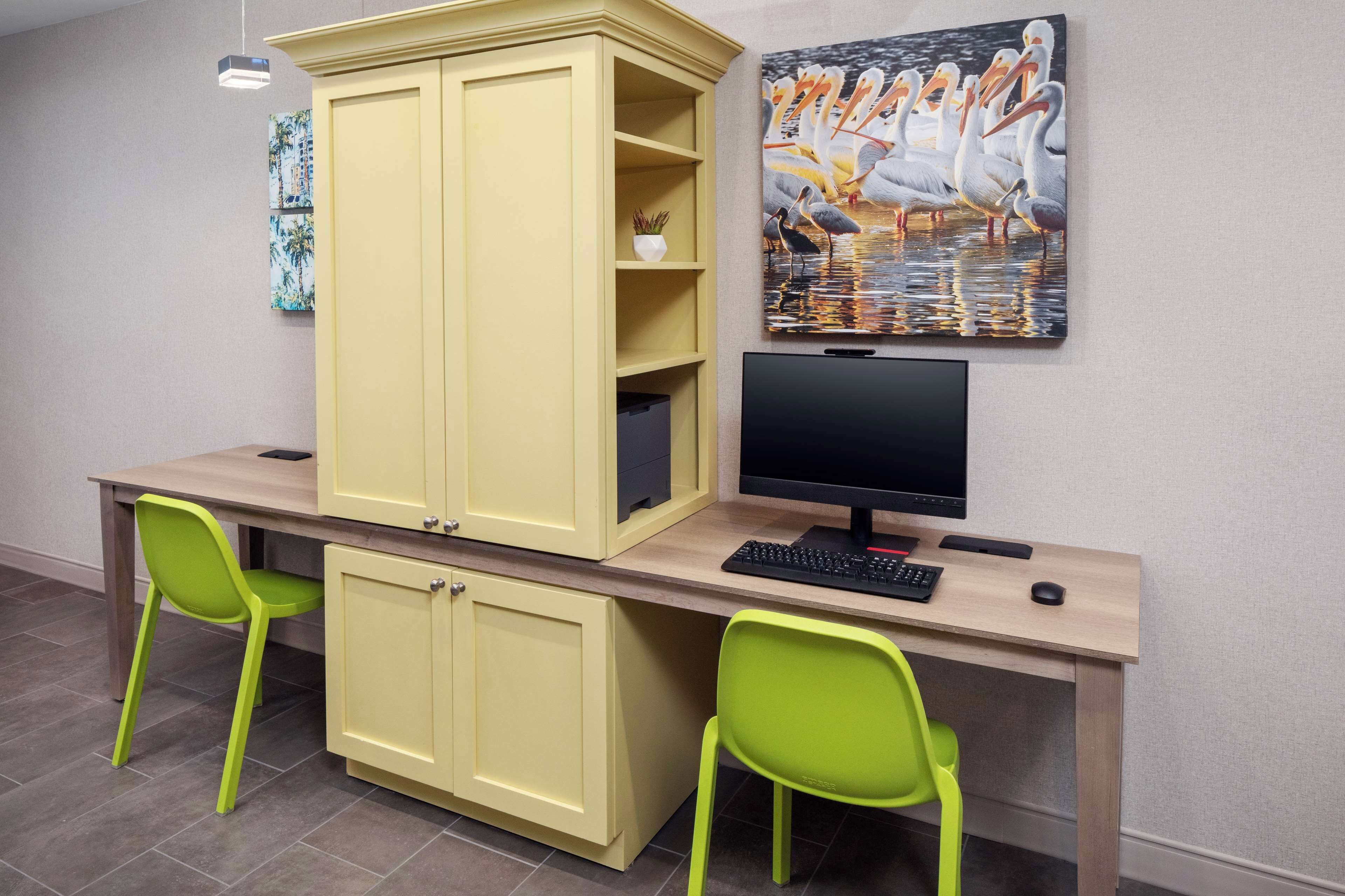 Un espacio de trabajo con un escritorio, dos sillas verdes, una computadora y un mueble grande.