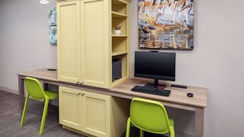 A study area with a desk, two green chairs, a computer, and a large cabinet.