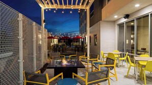 An outdoor dining area with yellow chairs and tables, string lights, and a fire feature. - Home2 Suites By Hilton Lake Mary Orlando (Lake Mary)