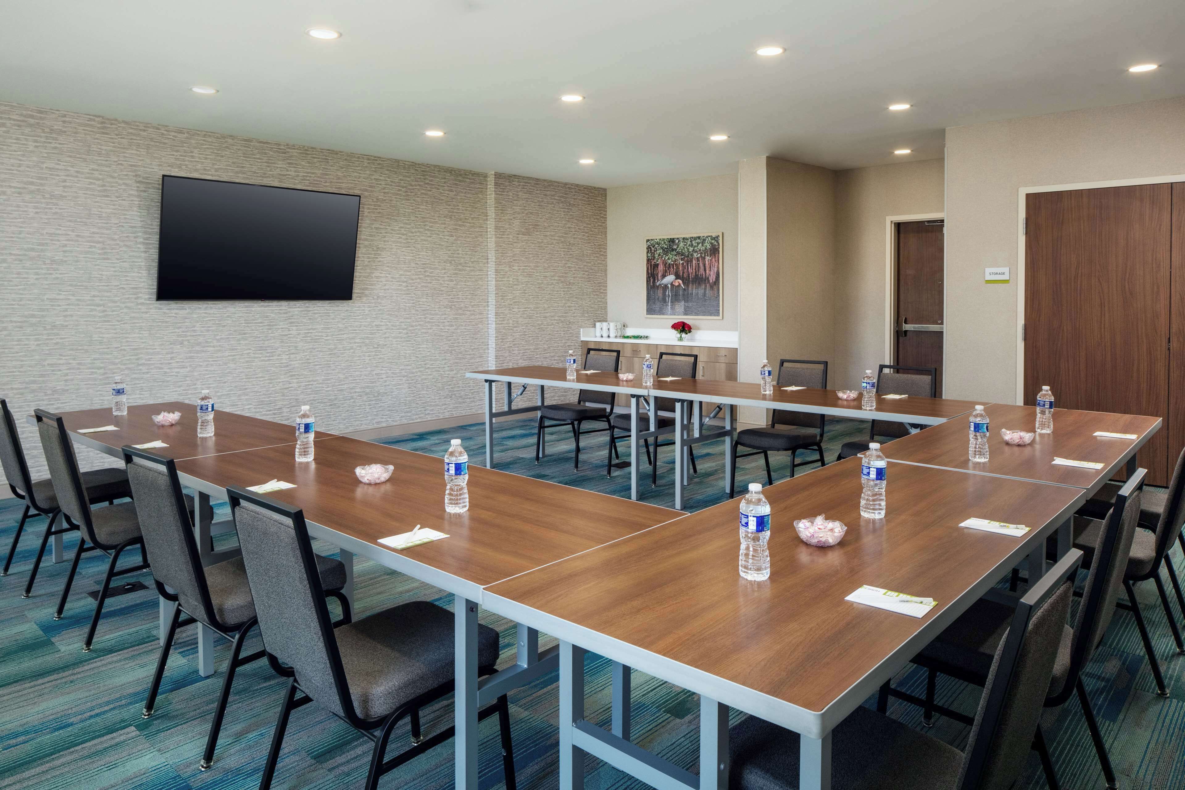A conference room with a long table, chairs, a flat-screen TV, and a painting on the wall.