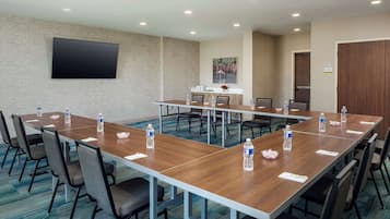 A conference room with a long table, chairs, a flat-screen TV, and a painting on the wall.