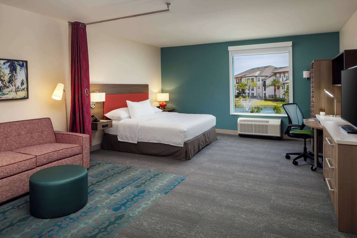 A hotel room with a bed, a desk, a chair, a couch, and a window with a view of buildings.