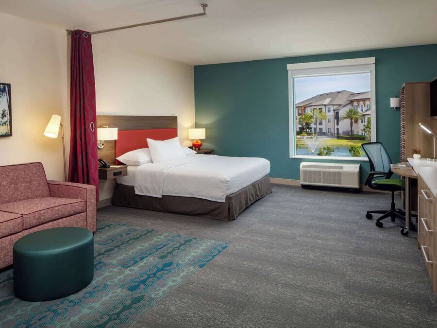 Ein Hotelzimmer mit Bett, Schreibtisch, Stuhl, einer Couch und einem Fenster mit Blick auf Gebäude.