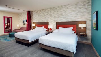 Et hotelværelse med to senge, en rød sengegavl, et lille bord, en stol og et spejl.