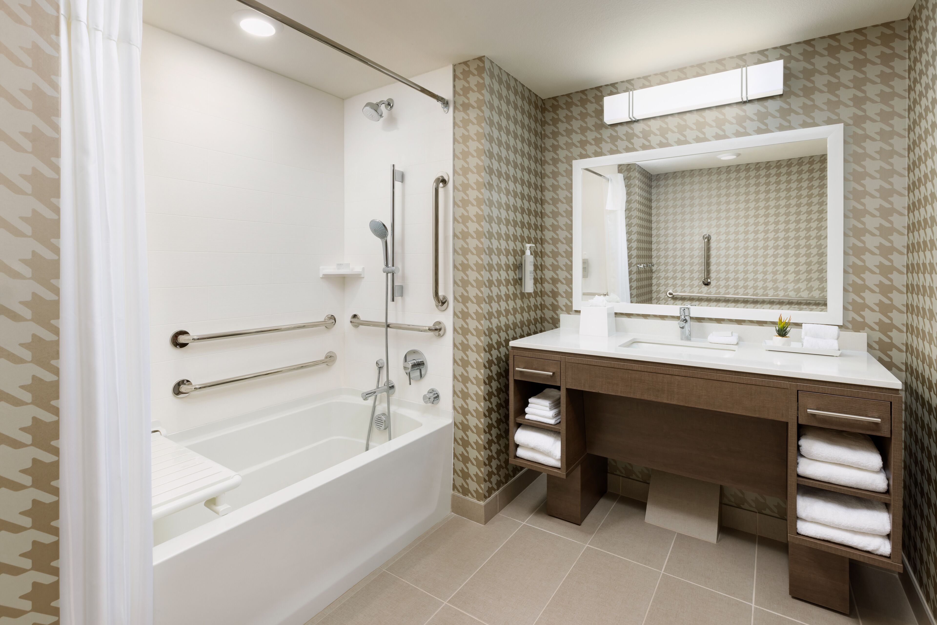 A modern bathroom with a walk-in shower, grab bars, a large mirror, and a vanity with towel racks.