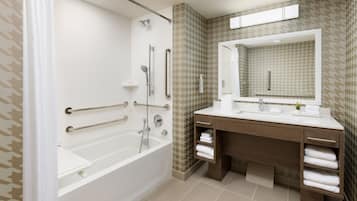 A modern bathroom with a walk-in shower, grab bars, a large mirror, and a vanity with towel racks.