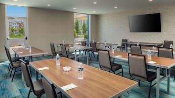 A conference room with multiple tables, chairs, water bottles, and a large flat-screen TV on the wall.