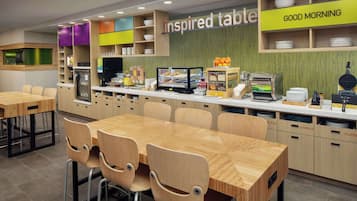Un'area colazione moderna con tavoli e sedie in legno, una vetrina con prodotti alimentari e un cartello con la scritta "inspired table".