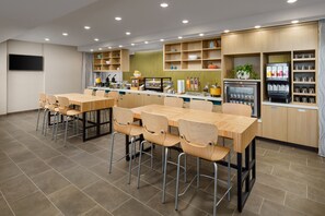 Un restaurante moderno con mesas y sillas de madera, una barra con máquina de café y estantes con diversos artículos.