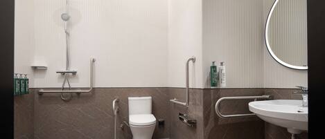 A modern bathroom with a toilet, shower, and sink, equipped with grab bars and a handrail.