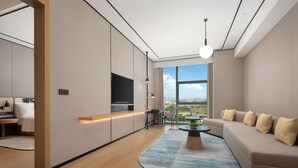 A modern living room with a large window, a sofa, a coffee table, and a TV mounted on the wall. - Hilton Garden Inn Shenzhen Guangming Hongqiao Park (Shenzhen)
