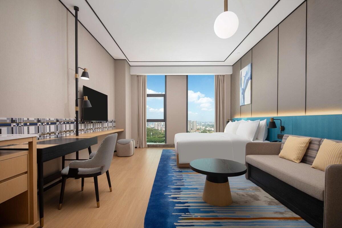 Una habitación de hotel moderna con una cama grande, un sofá, un escritorio y vistas a la ciudad.