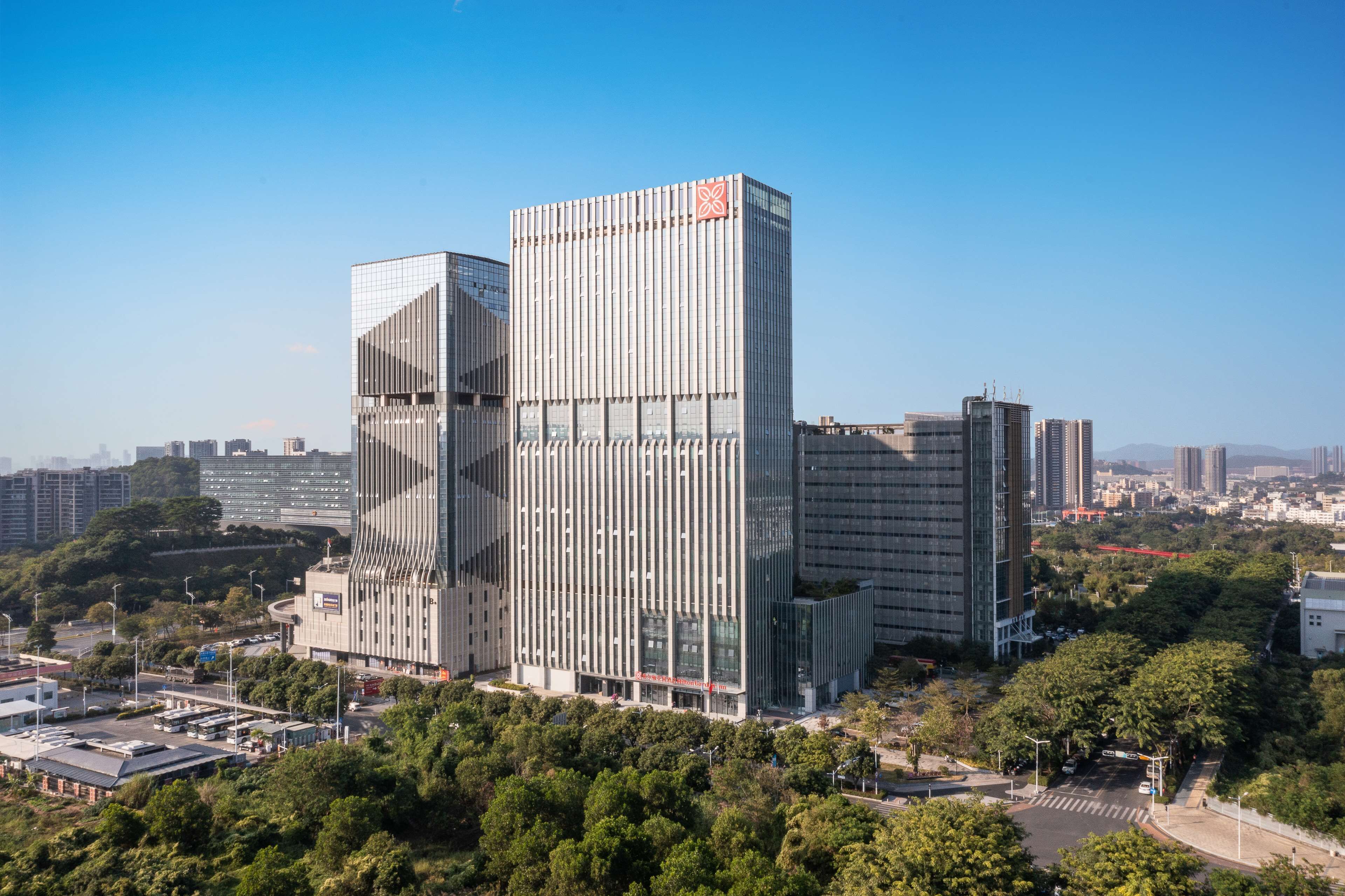 A modern high-rise building with a distinctive facade, surrounded by greenery and other urban structures.