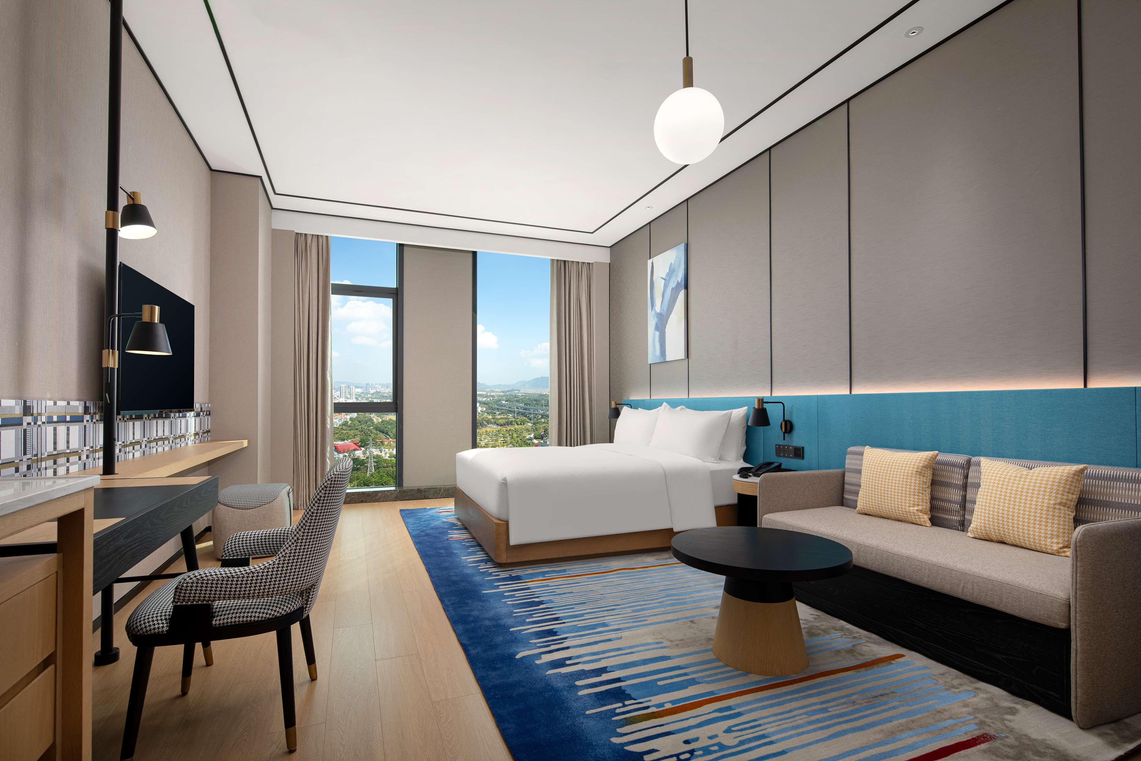 Une chambre d’hôtel moderne dotée d’un grand lit, d’un canapé, d’un bureau avec une chaise et offrant une vue sur la ville.
