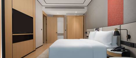 Een moderne hotelkamer met een groot bed, een televisie op een standaard, een nachtkastje met een lamp en een bureau met een telefoon.