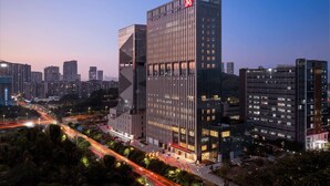A modern high-rise building with a prominent logo on the top, surrounded by other high-rise buildings and a busy road with light trails. - Hilton Garden Inn Shenzhen Guangming Hongqiao Park (Shenzhen)
