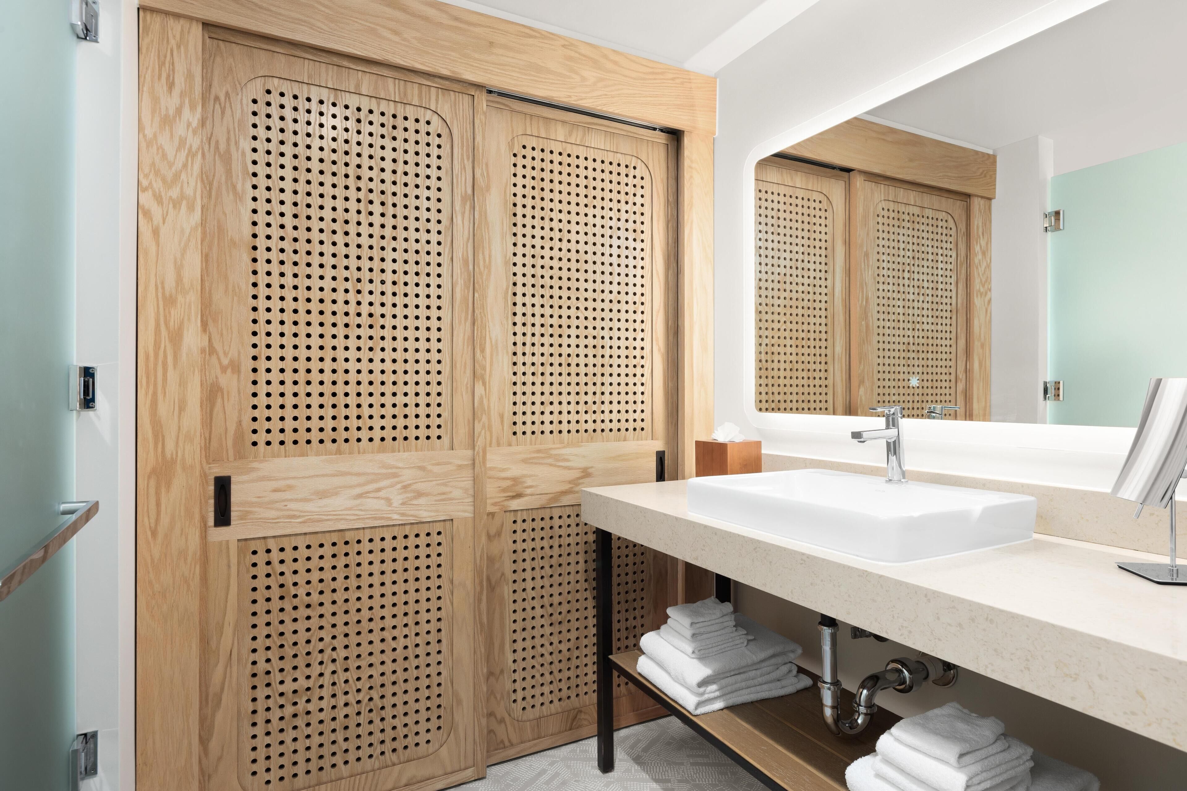 A modern bathroom with a wooden vanity, a large mirror, and a sink.