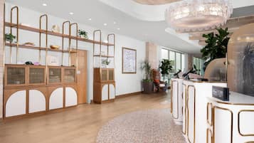 A hotel reception area with a wooden reception desk, a large chandelier, and a wall-mounted display.