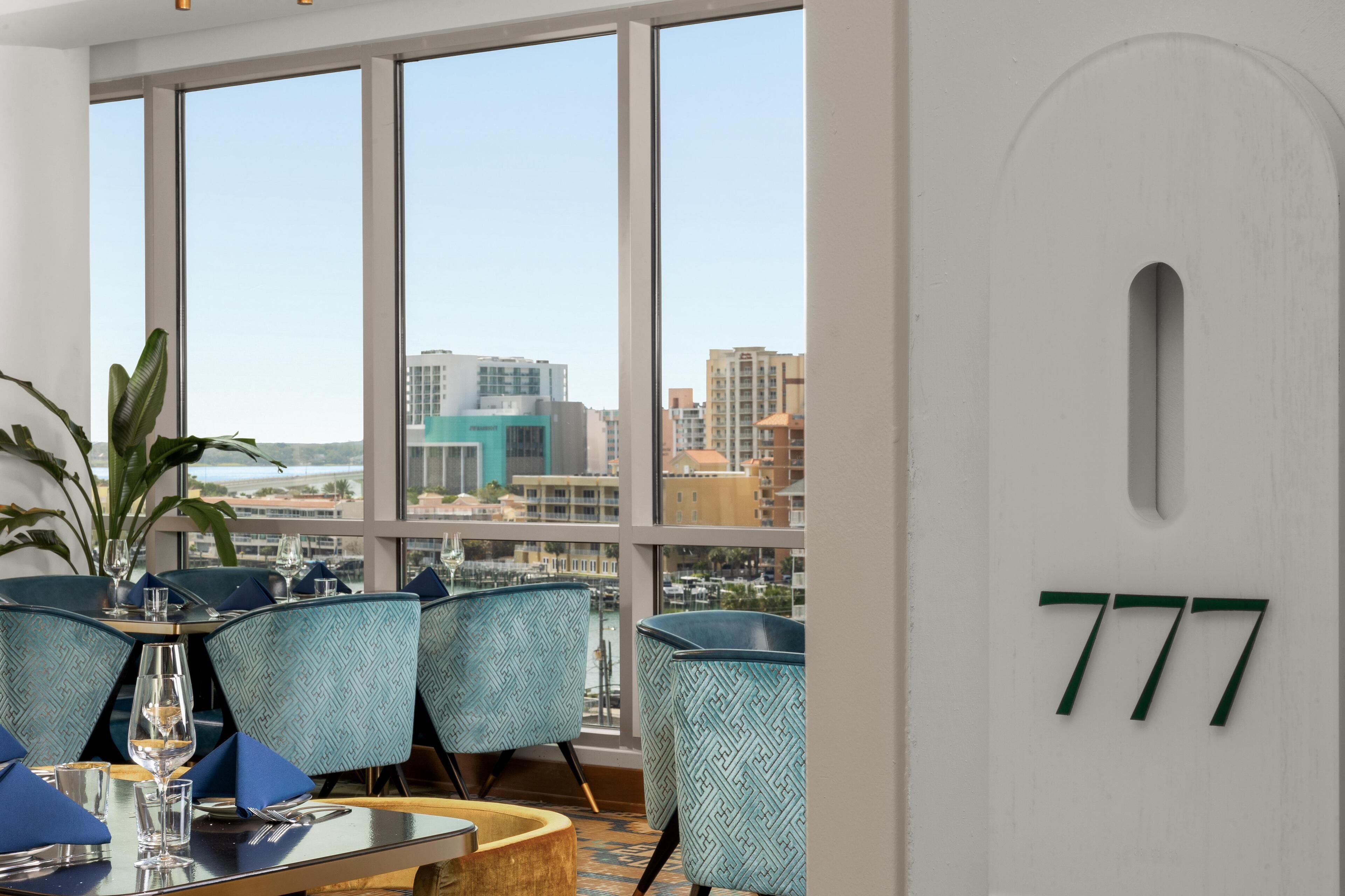 A dining area with a view of the city through large windows, patterned chairs, and a number sign on the wall.