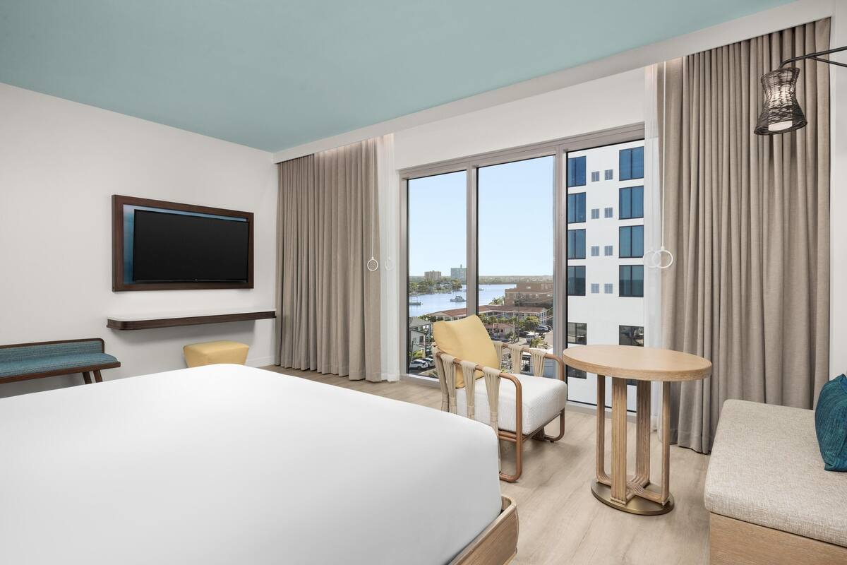 Een hotelkamer met een groot bed, een tv aan de muur, een klein tafeltje, een stoel en een bank.