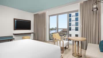 A hotel room with a large bed, a TV mounted on the wall, a small table, a chair, and a sofa.