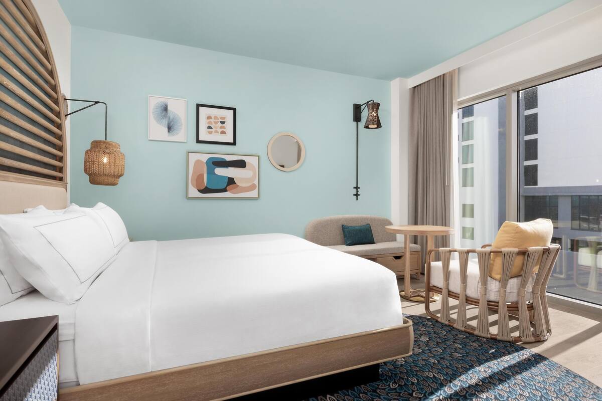 Een hotelkamer met een groot bed, een ronde spiegel, een rieten stoel en een klein tafeltje.