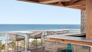 Een balkon met rieten stoelen en een bar, met uitzicht op een strand en de oceaan.