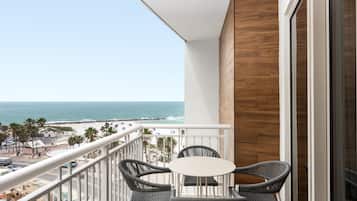 A balcony with a view of the beach and ocean, featuring wicker furniture and a white table.