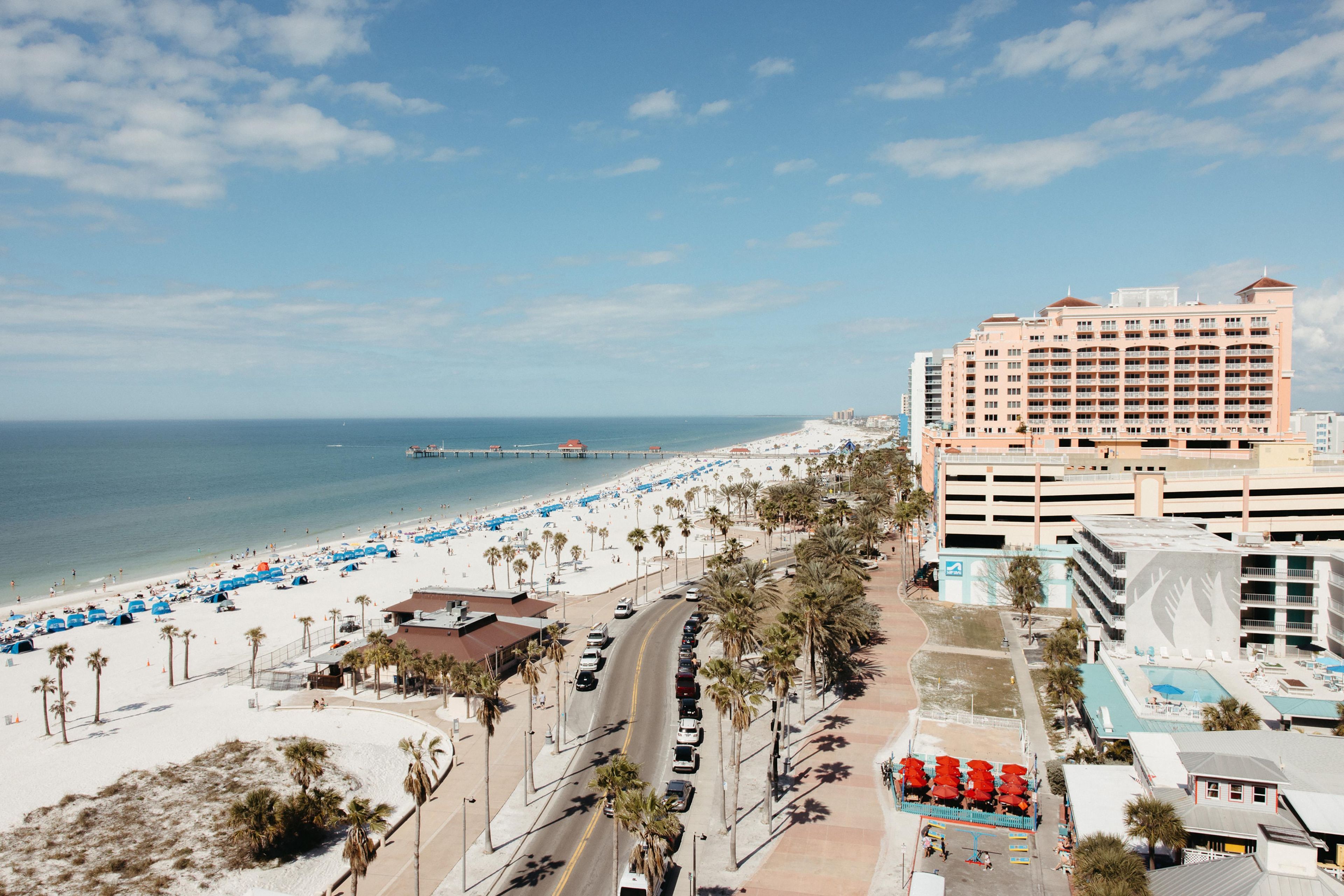 A coastal cityscape with a beachfront, a hotel, and a road with parked cars.