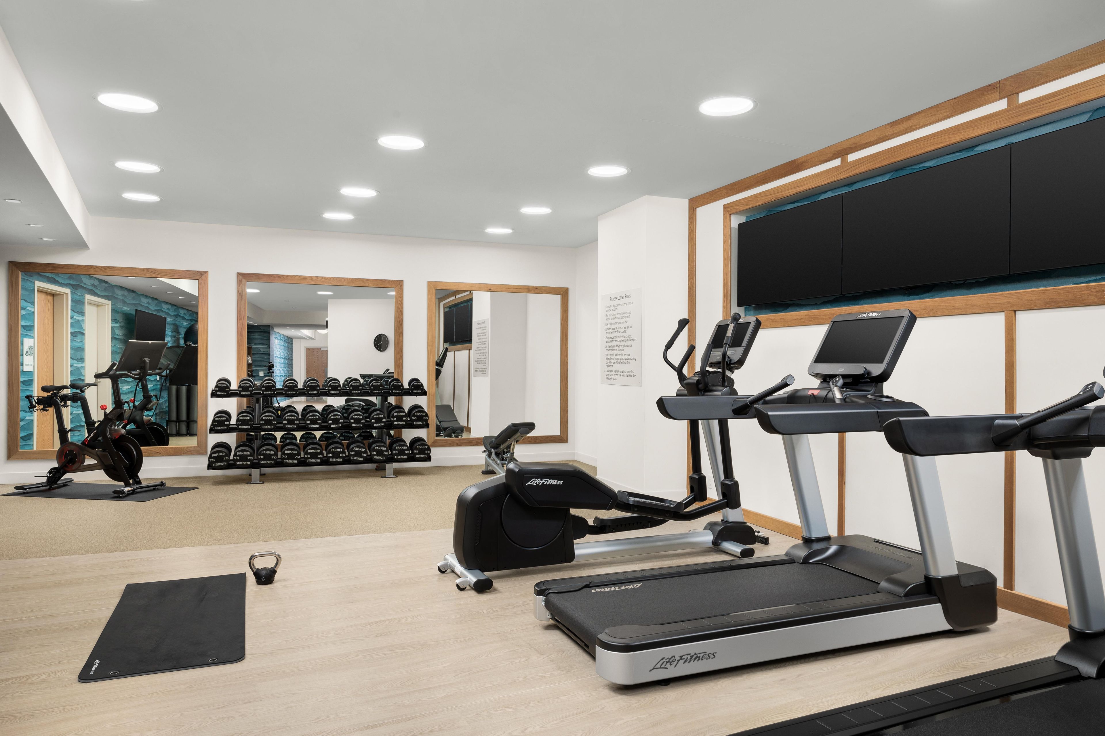 Un gimnasio con cintas de correr, bicicletas estáticas y pesas sueltas.