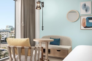 A modern hotel room with a view of the city, a sofa, a small round table, and a chair with a woven backrest. - The Hiatus Clearwater Beach, Curio Collection By Hilton (Clearwater Beach)