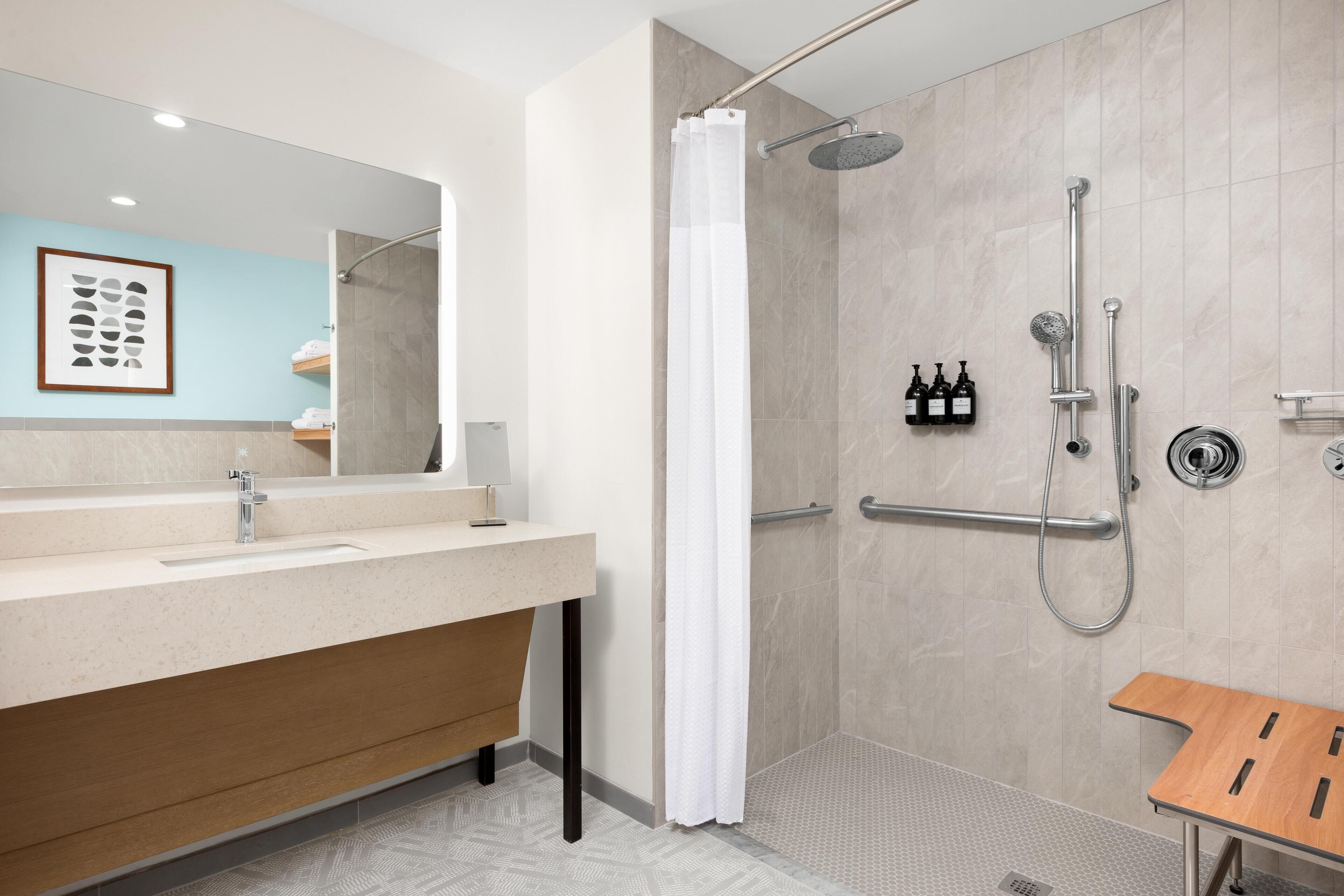 Un baño moderno con ducha, tocador con espejo y banco de madera.