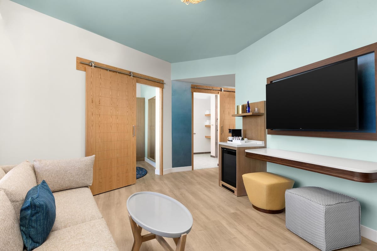 Een moderne woonkamer met een bank, een salontafel, een televisie en een keukenhoek met een koelkast en een spoelbak.