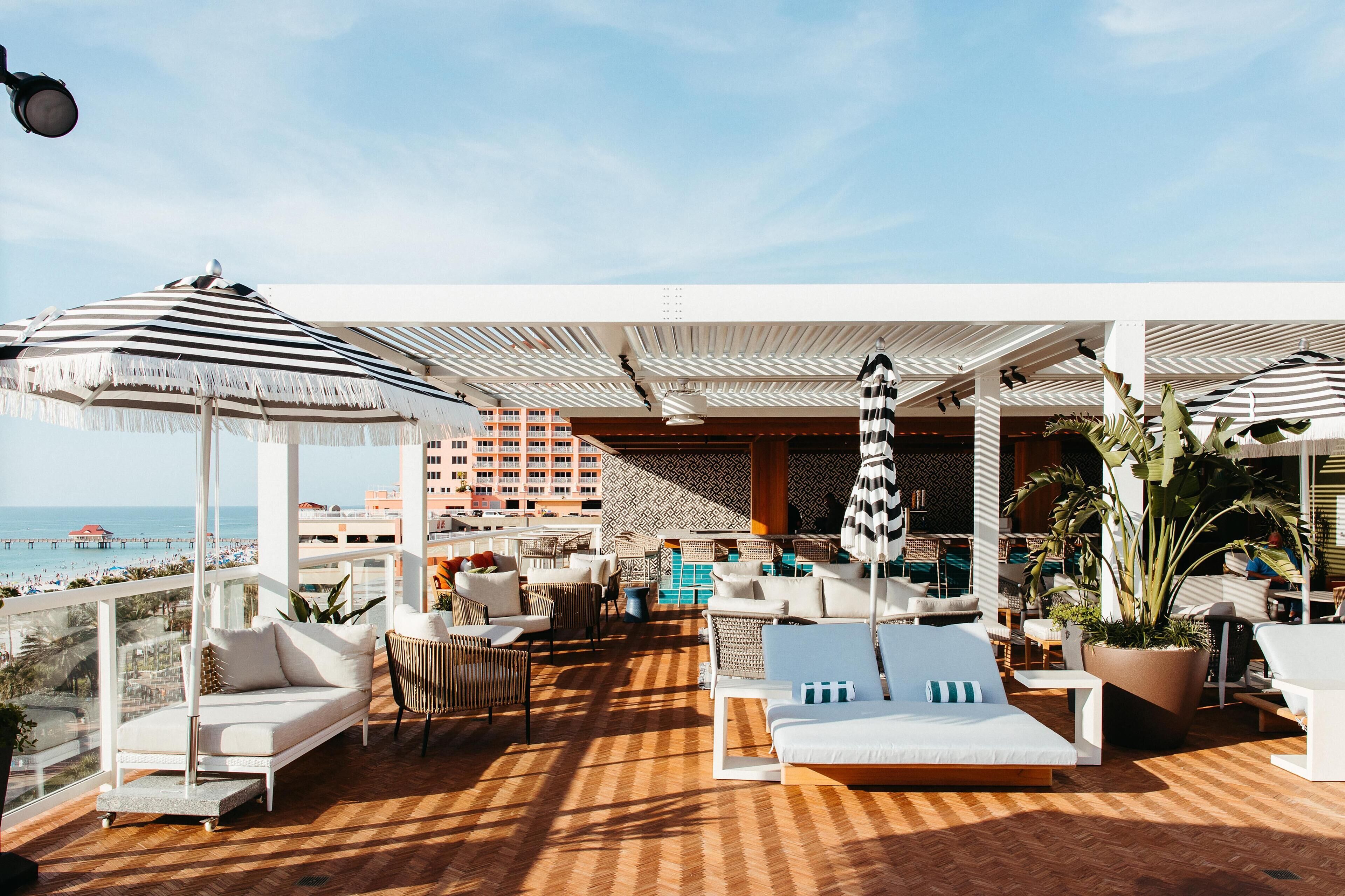 Un salon sur le toit avec des espaces de détente en plein air, une piscine et une vue sur la plage.