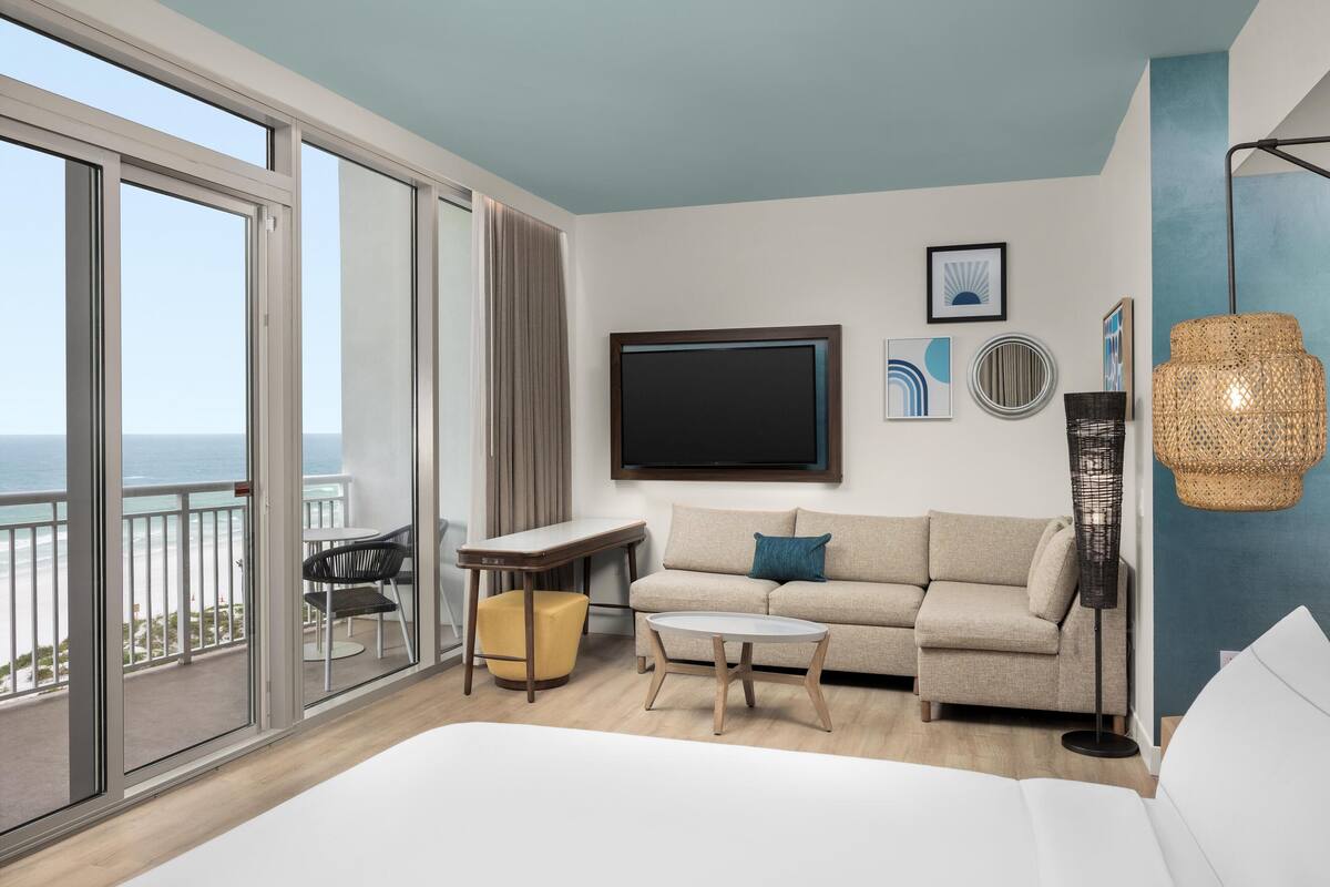 Een moderne hotelkamer met een balkon, een bank, een kleine tafel, een televisie en een rieten lamp.