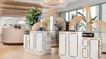 A modern hotel lobby with a large plant, a round seating area, and a chandelier.
