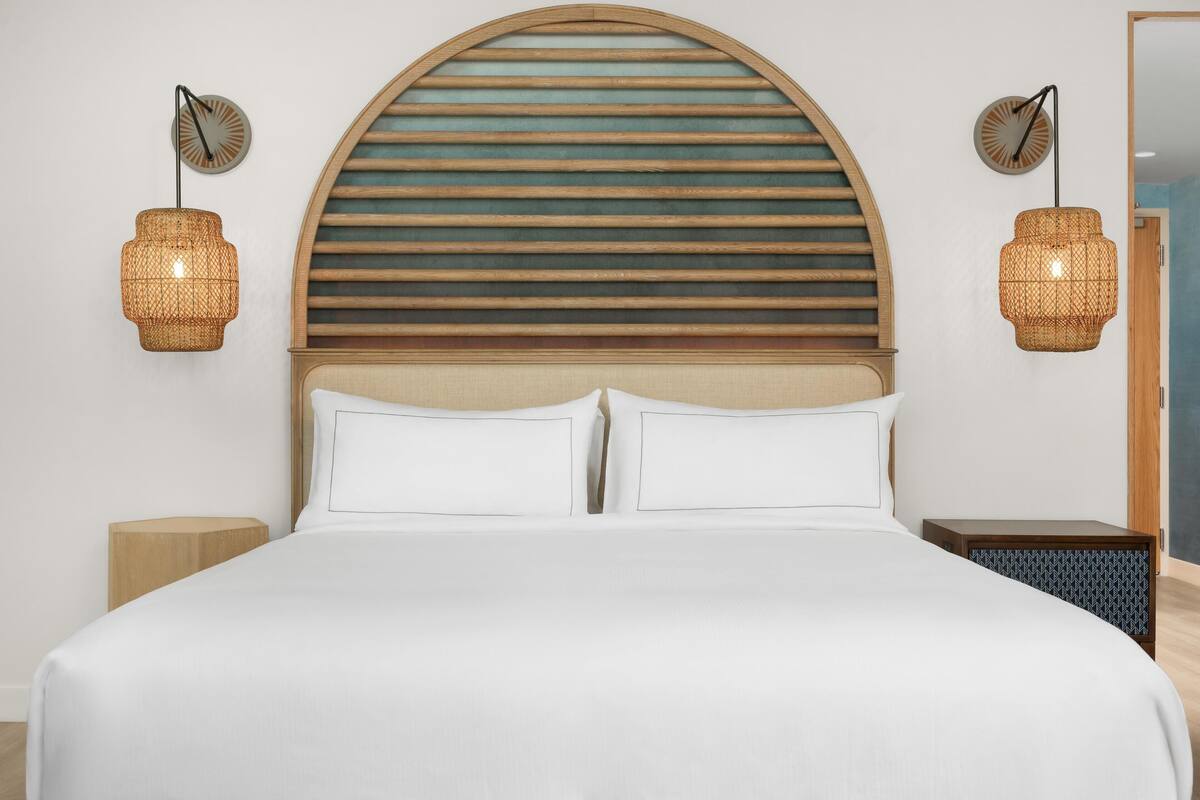 Een bed met witte lakens, een houten lattenbalken hoofdeinde en twee wandlampen van riet.