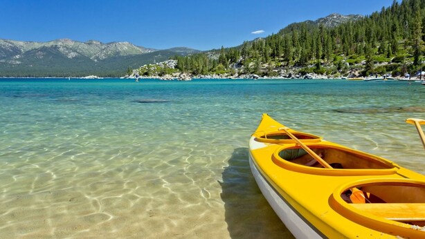 A clear lake with a yellow canoe and a person paddling, surrounded by mountains and trees. - Modern Private Retreat Near Riverwalk District!
 (Reno)