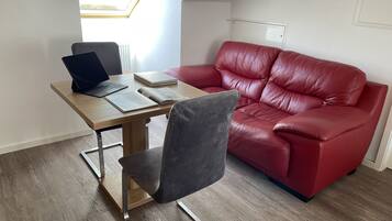 Una habitación moderna con un escritorio de madera, una computadora portátil, un libro abierto, un sofá de cuero rojo y un tragaluz.