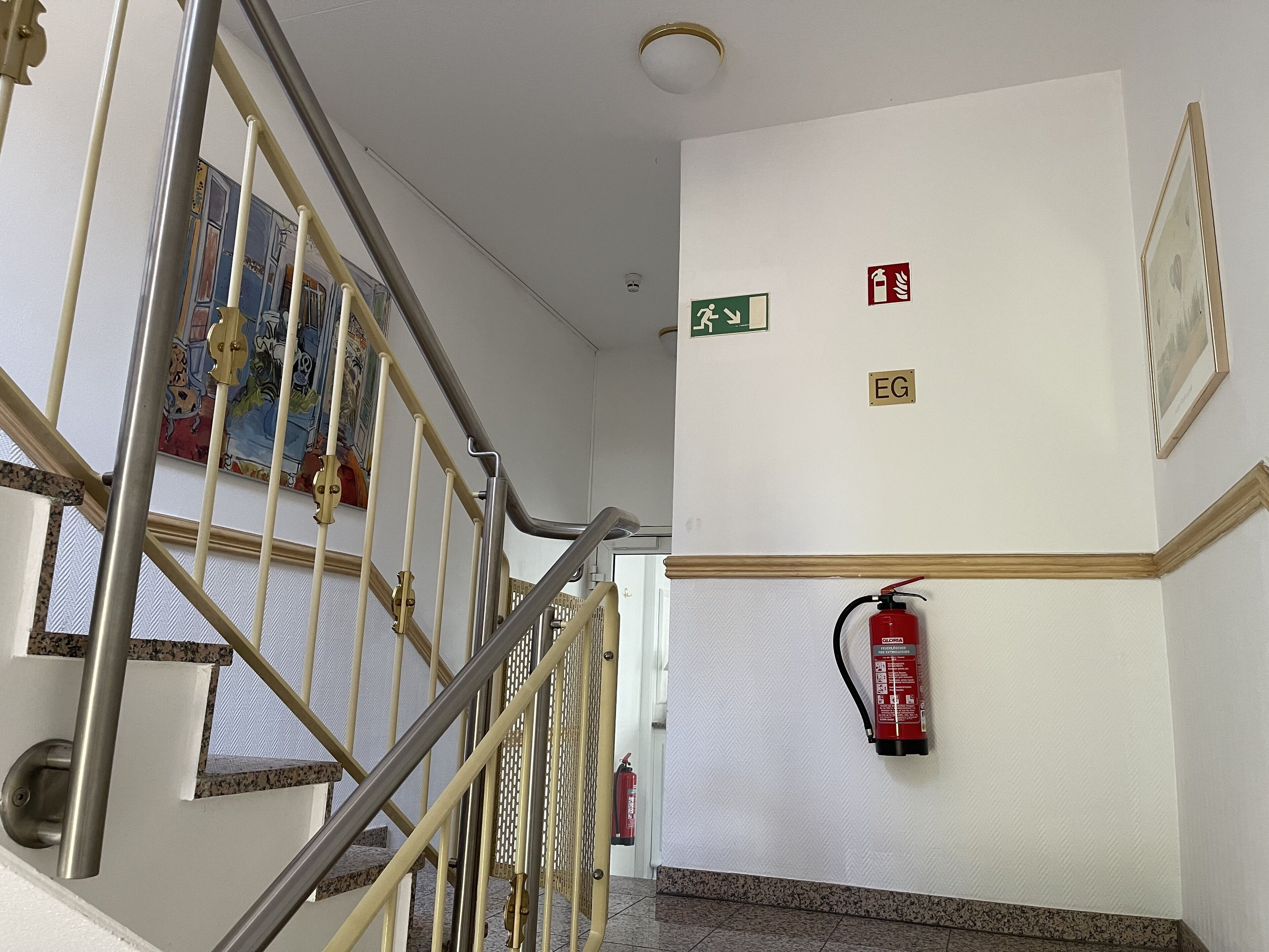A staircase with metal railings, a fire extinguisher mounted on the wall, and a green emergency exit sign.