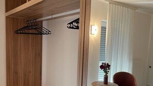 A room with a wooden wardrobe, a mirror, a small table with a vase, and a red chair. - Eurotel am Main (Offenbach am Main)