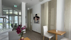 A modern hotel lobby with a wooden table, two white chairs, a vase with flowers, and a large window with a view of the outside. - Eurotel am Main (Offenbach am Main)