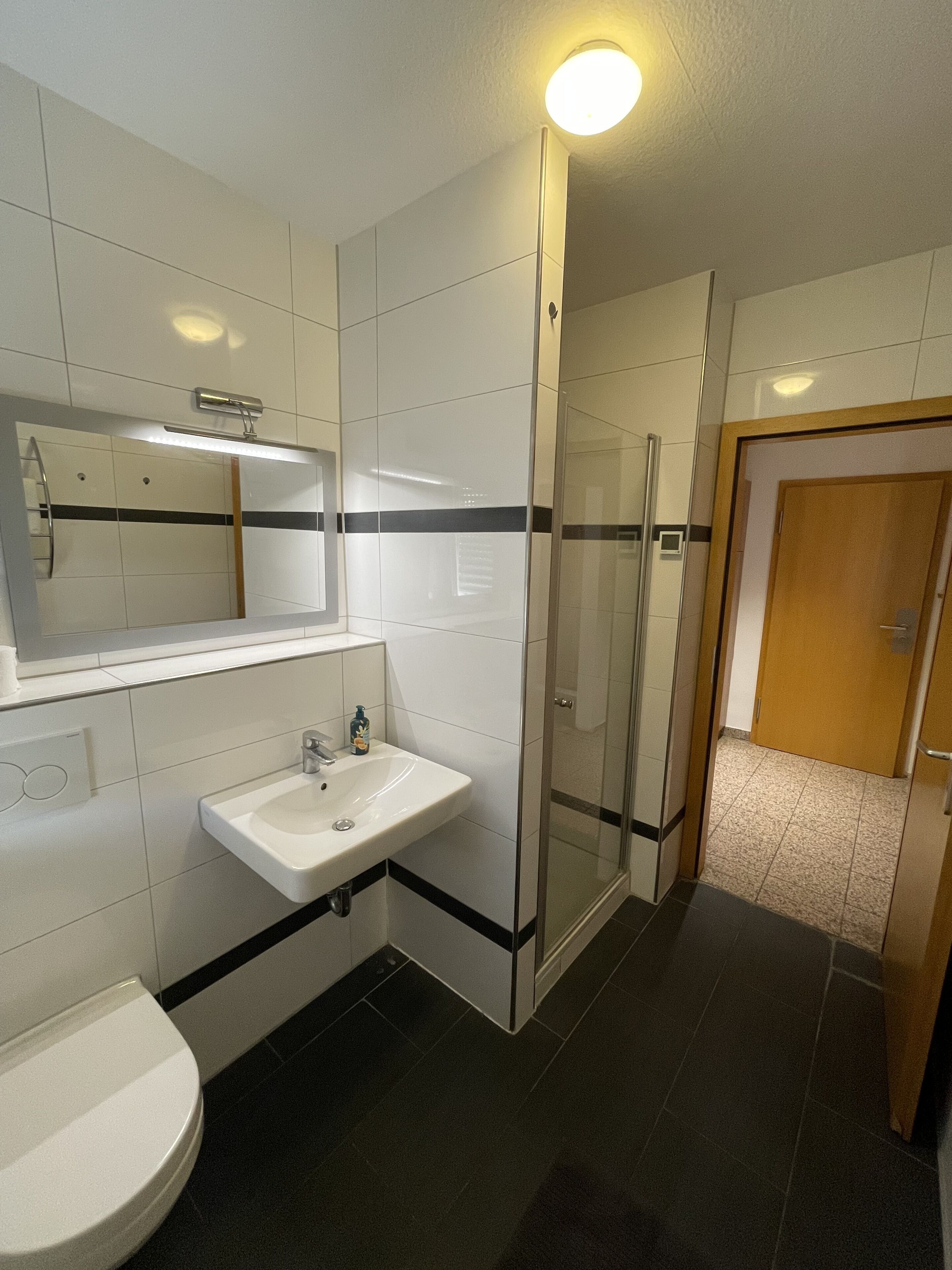 Un baño moderno con lavamanos blanco, espejo y zona de ducha.