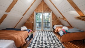 A cozy attic bedroom with two beds, a large window, and a wooden ceiling.