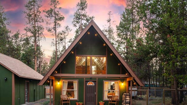 A cabin with a triangular roof, large windows, and a porch with chairs.