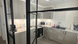 A modern kitchen with a glass partition, stainless steel appliances, and light wood flooring. - House by the Sea, Worthing. (Worthing)
