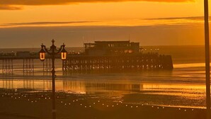 A pier extending into calm waters with a building on it and street lamps in the foreground. - House by the Sea, Worthing. (Worthing)