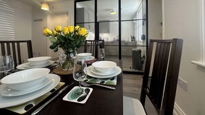A dining area with a table set for four, a vase with yellow flowers, and a view into the kitchen through a glass door. - House by the Sea, Worthing. (Worthing)