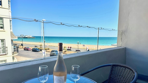 A balcony with a table, a bottle of wine, two glasses, and a bowl of olives. The view includes a beach and the ocean. - House by the Sea, Worthing. (Worthing)