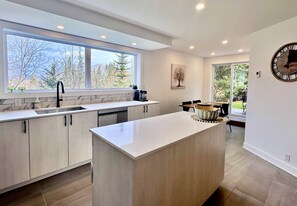 Cocina moderna con una isla grande, lavavajillas integrado y ventana con vistas a un bosque.